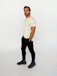 Man wearing a white t-shirt and black pants on a light gray background