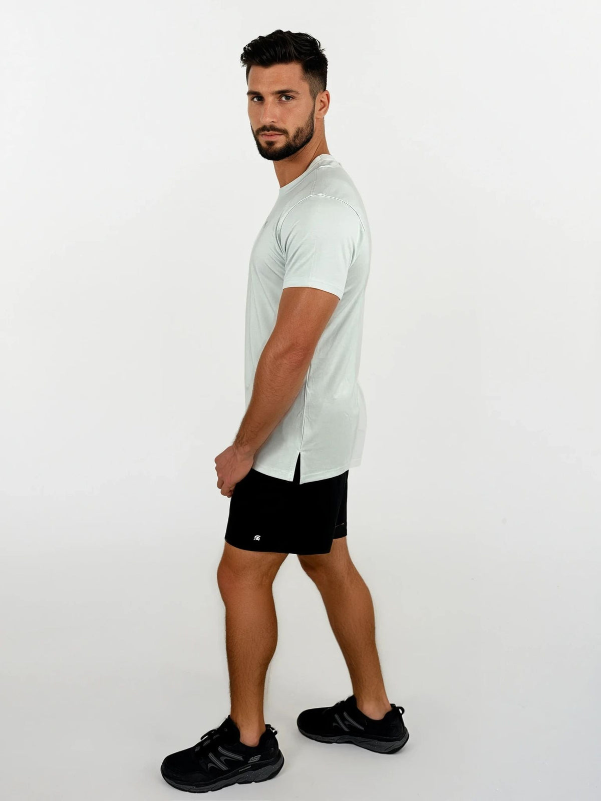 Man wearing a light gray t-shirt and black shorts on a white background