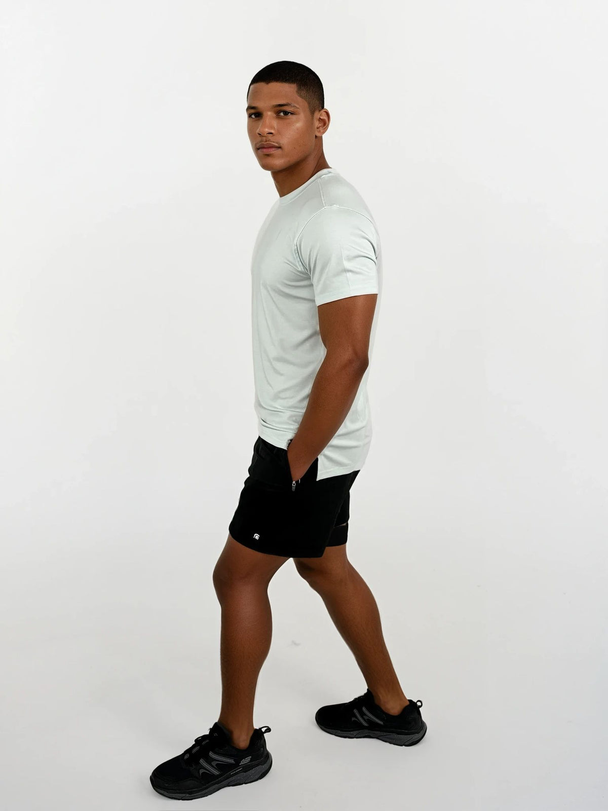 Man wearing a white t-shirt, black shorts, and black shoes on a white background